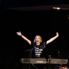 Eden at piano, wearing black t shirt, arms outspread